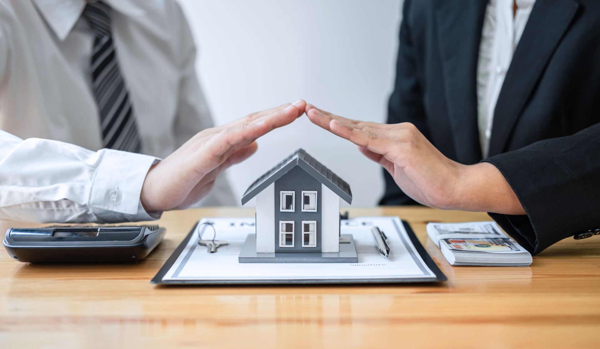 Sicherer Immobilienkauf in Bautzen | Immobilien Anders GmbH Zwei Hände schützen symbolisch ein Hausmodell über einem Vertrag in Bautzen. Immobilien Anders GmbH – Ihr sicherer Partner für Immobilien.